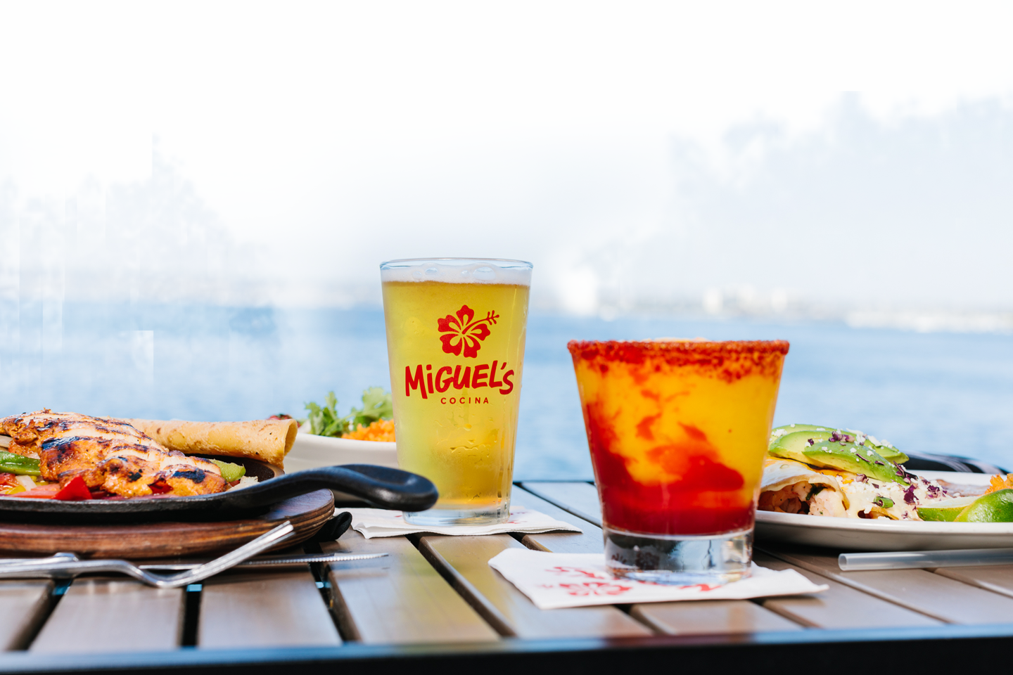 seaside view from a table at miguels. foreground of plate of food and a glass of beer next to a cocktail