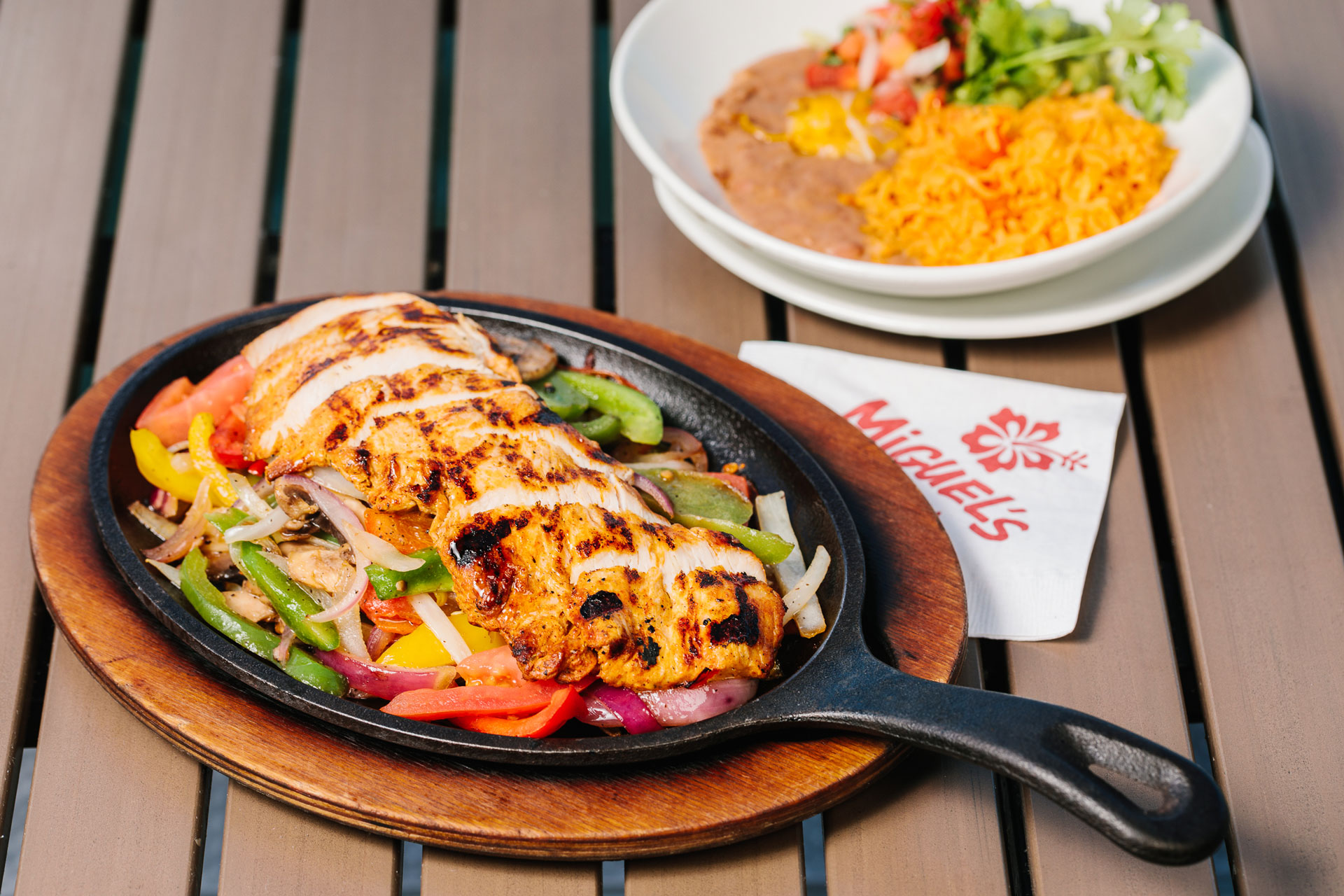 skillet of miguels chicken fajitas with plate of rice and beans