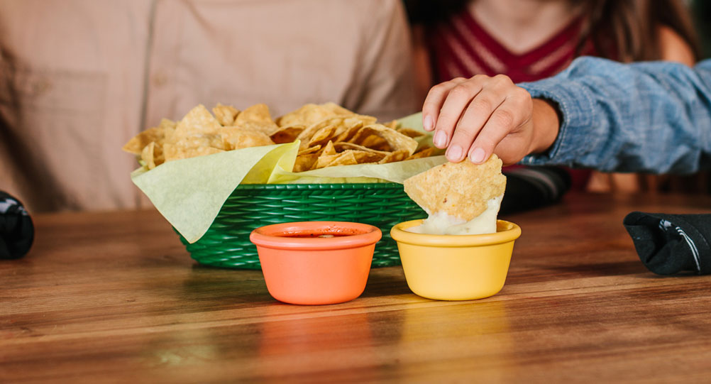 basket of chips with kids hand dunking a chip into creamy jalapeño white sauce